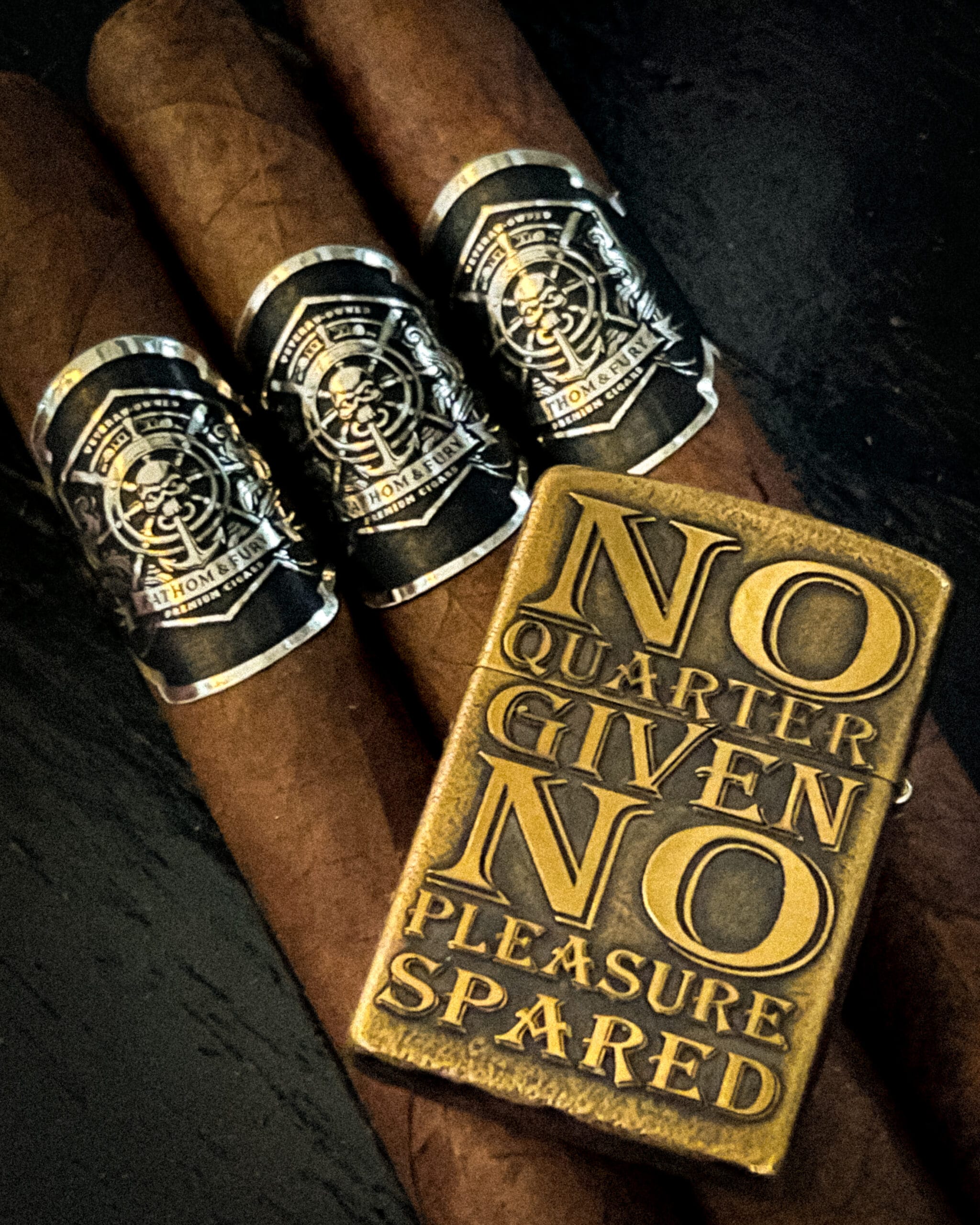Three banded Fathom & Fury cigars beside the No Quarter Given brass lighter